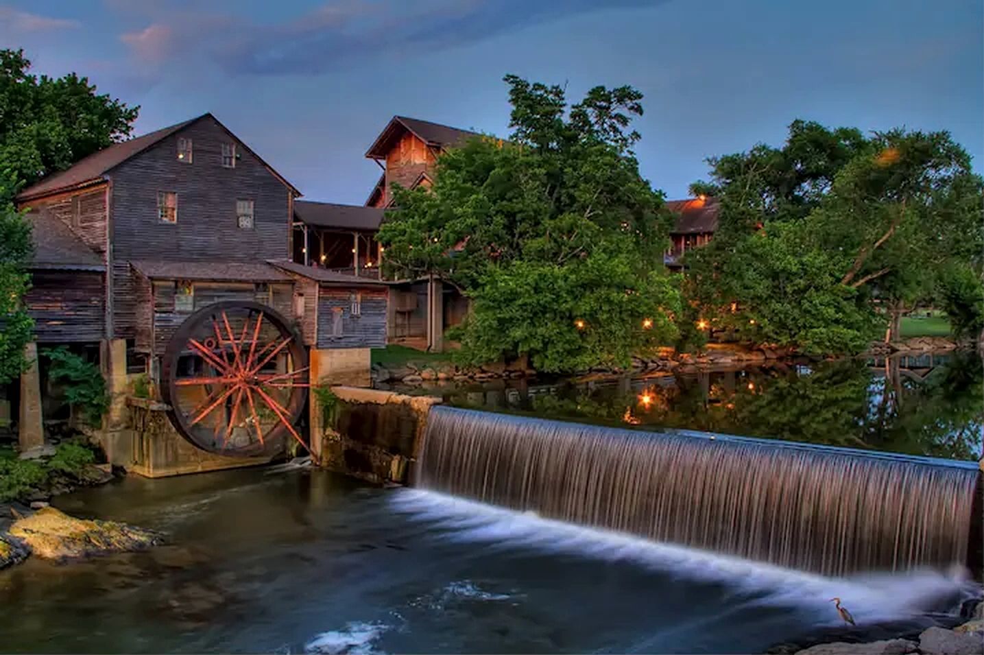 Un molino histórico con una noria grande, edificios de madera y una cascada.