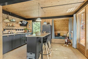 A modern kitchen with wooden accents, a central island, bar stools, and a cozy seating area with a view. - 70s holiday home with views of Mols Bjerge (Ebeltoft)