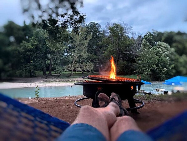 A person relaxing on a hammock with a campfire in the background.