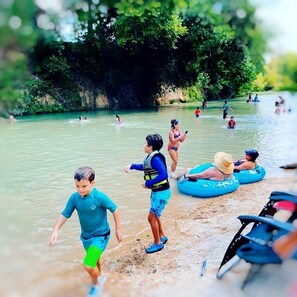 A river with people swimming and floating, surrounded by greenery.