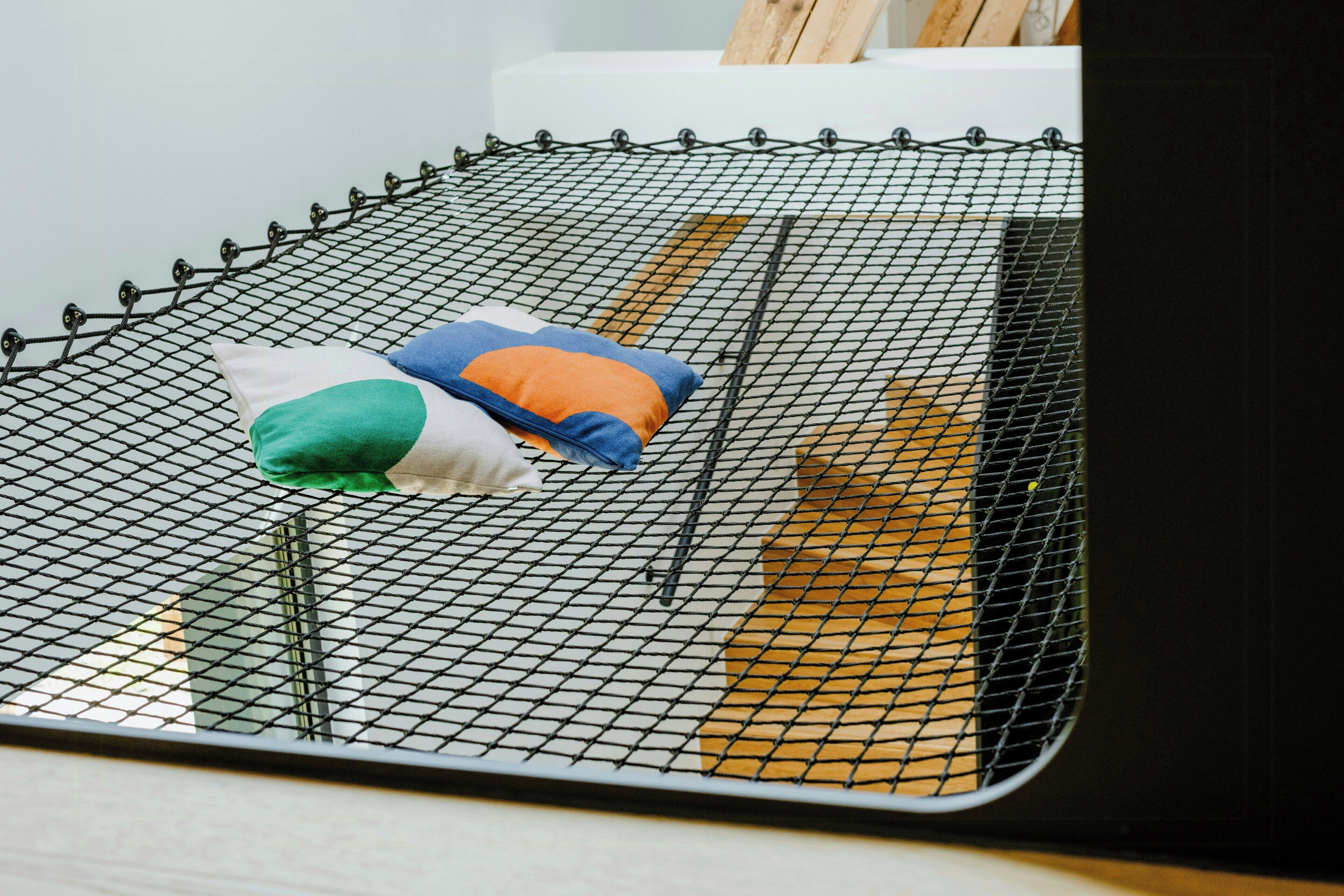 Ein Bett mit einem Metallschutznetz, einem Kopfkissen und einem hölzernen Kopfteil.