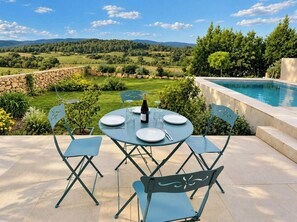 Un área de comedor al aire libre con una mesa dispuesta para cuatro personas, una botella de vino y una piscina al fondo.