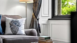 Um quarto com sofá, luminária, janela com cortinas e mala sobre uma mesa.