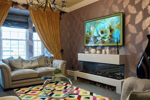 A living room with a sofa, a glass coffee table, a fireplace, and a large painting on the wall.