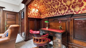 Una habitació amb una cadira de pell vermella, un escriptori amb calaixos, una làmpada i un fons de pantalla estampat.