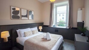 Hotellihuone, jossa on sänky, yöpöytävalaisimet, ikkuna verhoilla, patteri ja seinälle kiinnitetty peili.