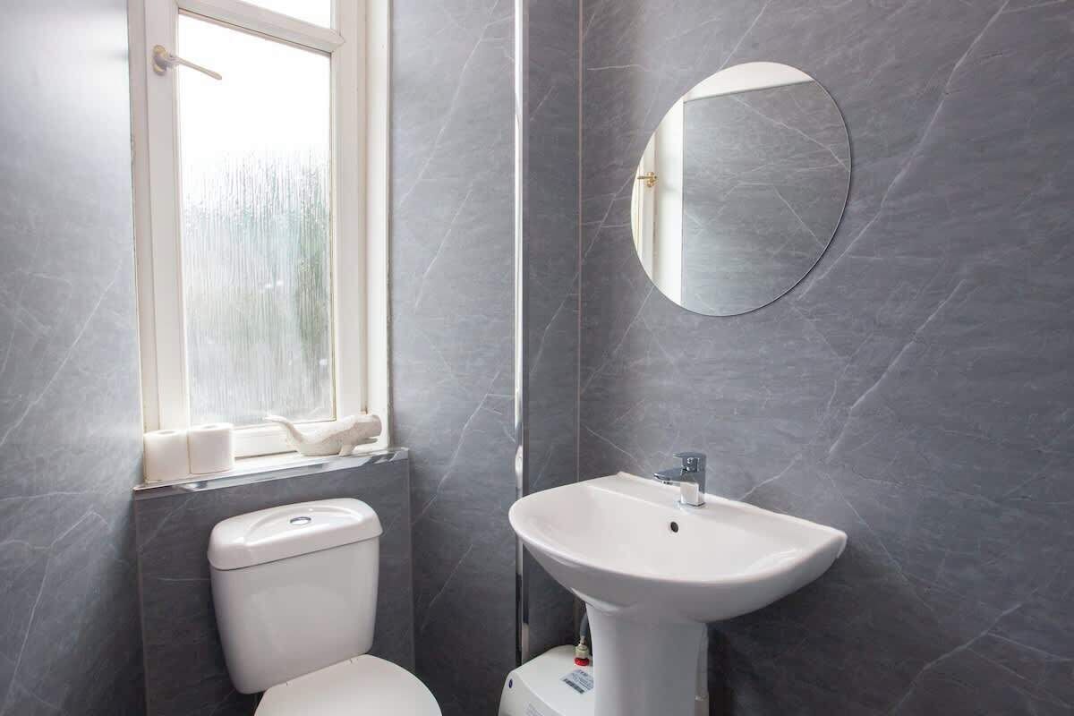 A bathroom with a toilet, a sink, a mirror, and a window.