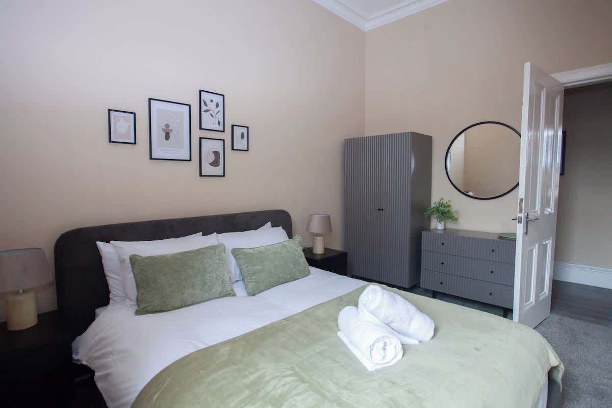 A neatly made bed with pillows, a bedside lamp, a dresser, a mirror, and framed pictures on the wall.