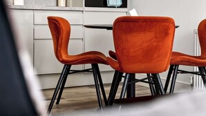 A modern kitchen with white cabinets, a black oven, and a dining area with orange chairs. - Modern City Apartment Just off Buchanan St (Glasgow City)