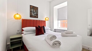 A neatly made bed with white linens, a red headboard, and two wall-mounted lamps. - Modern City Apartment Just off Buchanan St (Glasgow City)
