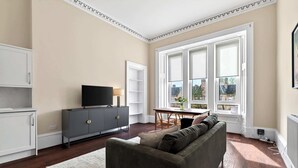 Ein Wohnzimmer mit grauem Sofa, Fernseher, Esstisch und einem großen Fenster mit Blick.