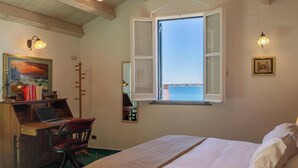 Une chambre à coucher avec un lit, un bureau avec un ordinateur portable, une chaise, une fenêtre donnant sur un beau paysage et un tableau accroché au mur.
