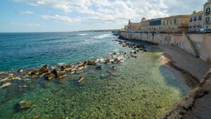 Une vue côtière avec une eau limpide, une côte rocheuse et des bâtiments historiques qui bordent la mer.