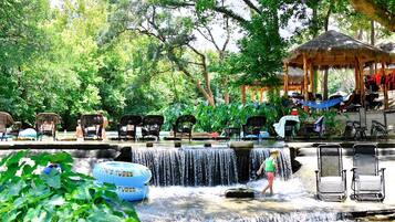 A water feature with chairs and a gazebo in a lush, green setting.