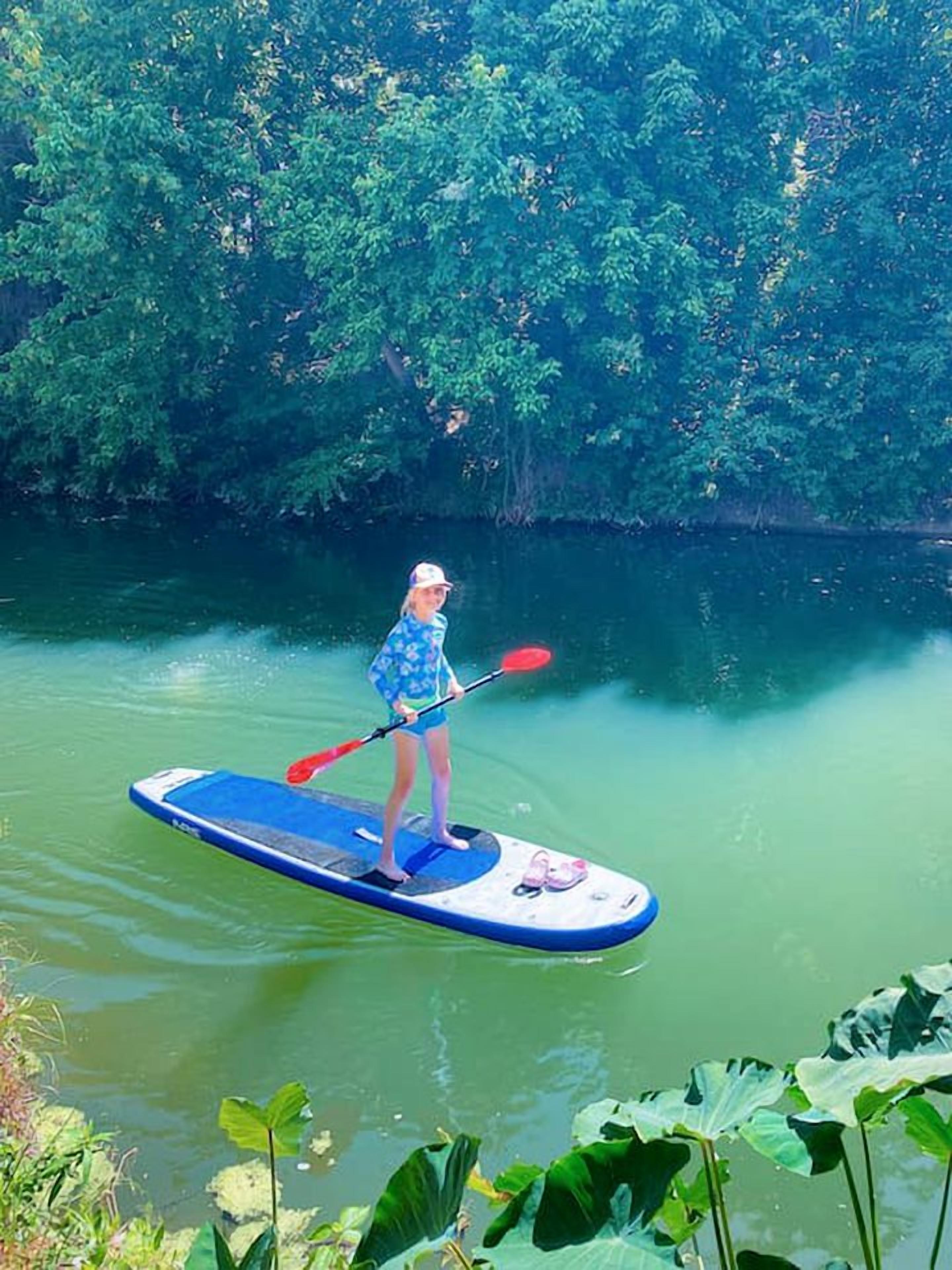 A person on a paddleboard in a body of water surrounded by dense greenery.