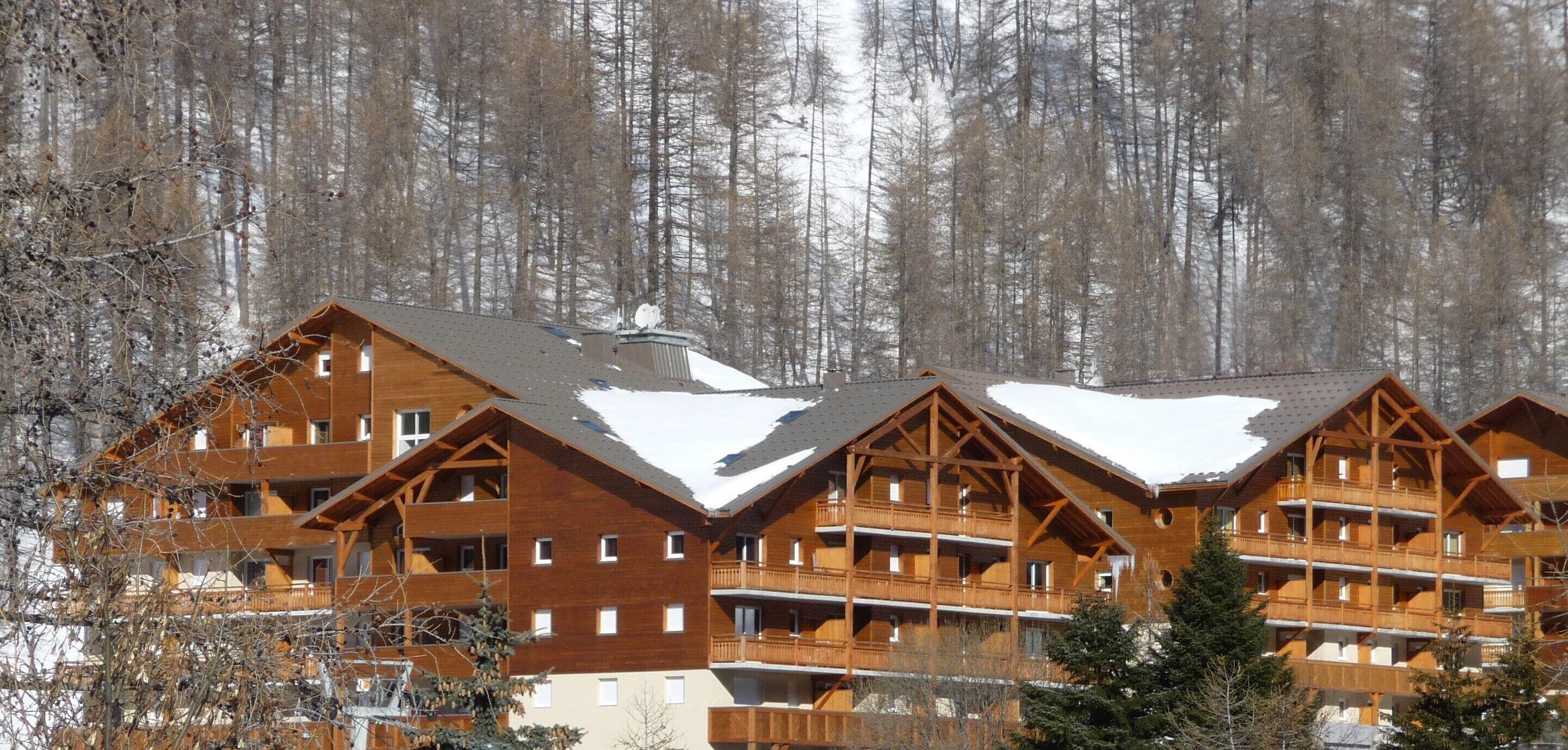 A multi-story wooden lodge with balconies, set against a snowy forest backdrop.