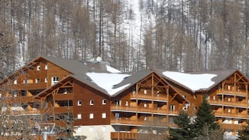 A multi-story wooden lodge with balconies, set against a snowy forest backdrop.
