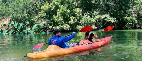 Dos personas hacen kayak en un río tranquilo rodeado de abundante vegetación.