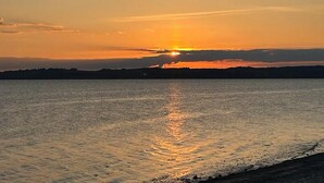 Ein Sonnenuntergang über einem Gewässer mit einer unscharfen Silhouette der Küste.