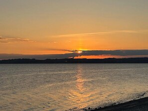 Ein Sonnenuntergang über einem Gewässer mit einer unscharfen Silhouette der Küste.