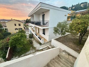 Ein modernes, zweistöckiges Gebäude mit Balkon, umgeben von Grünflächen und weiteren Wohnhäusern.