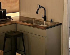 A compact kitchen with a single sink, a stool, and a microwave.