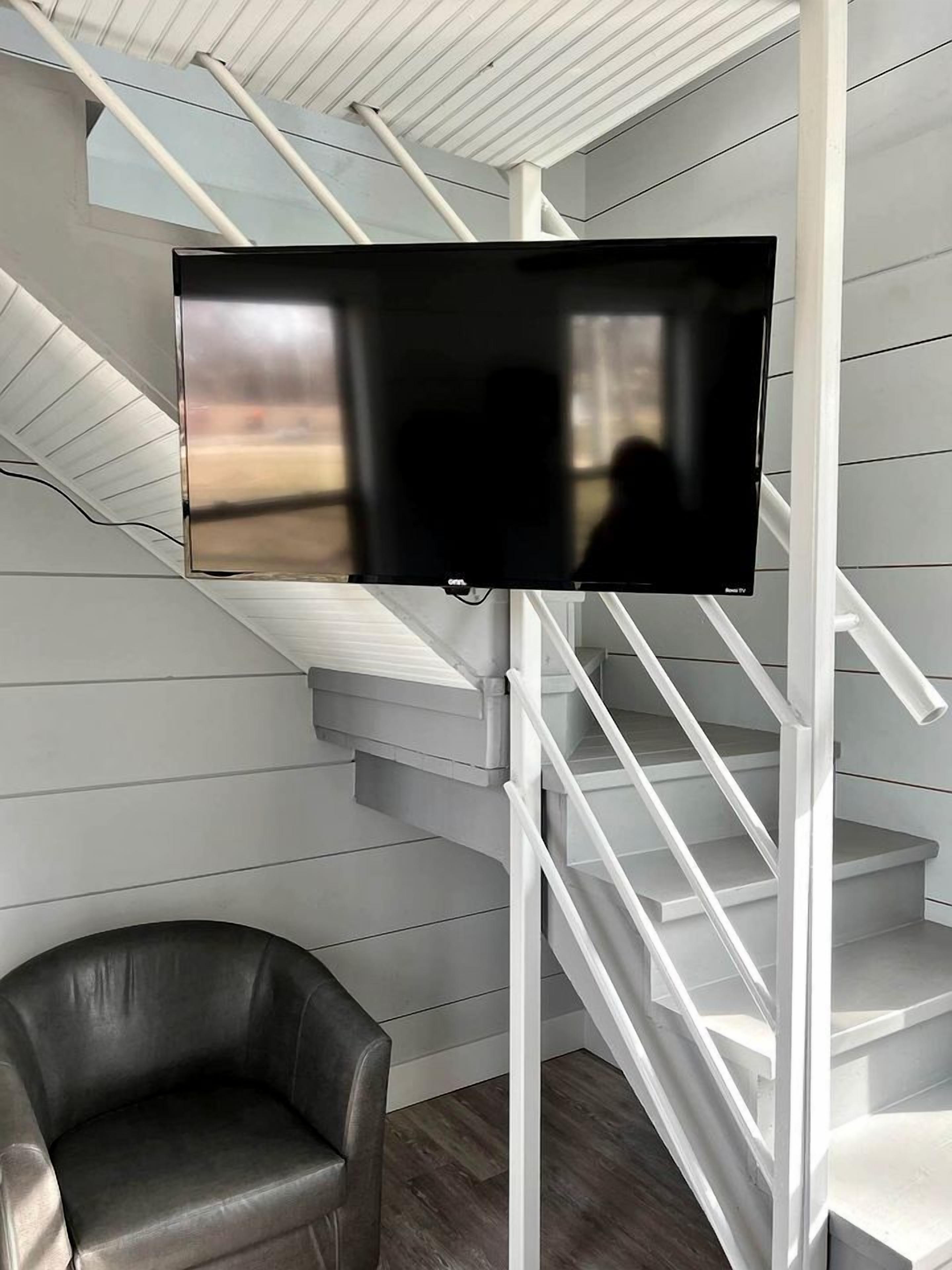 Un intérieur moderne avec un téléviseur à écran plat fixé sur un escalier blanc, un fauteuil en cuir et une vue sur l’extérieur.