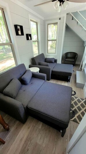 Un salon moderne avec un canapé d’angle, une petite table blanche et un escalier menant à un niveau supérieur.