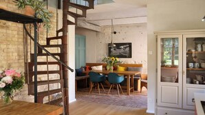 Un espace repas comprenant une table en bois, des chaises, un banc et un escalier.