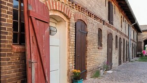 Une rue pavée, un bâtiment en briques avec une porte rouge et un petit jardin fleuri.