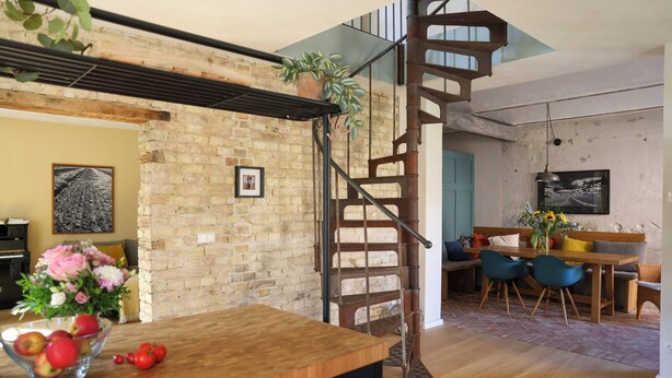 Un espace repas comprenant une table en bois, des chaises, un escalier et un mur en briques.