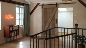 Une pièce avec un plancher en bois, une bibliothèque, un panneau lumineux au néon, une porte coulissante de style grange et un escalier avec une rampe noire.