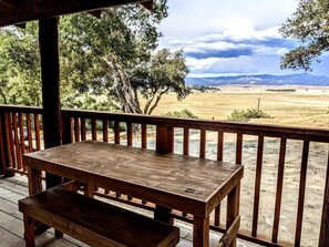 Eine Holzterrasse mit Tisch und Bank, mit Blick auf eine Wiese und ferne Berge.