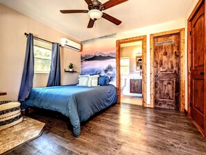 Ein Schlafzimmer mit Bett, Holzboden, Deckenventilator und Blick auf eine Berglandschaft durch ein Fenster.