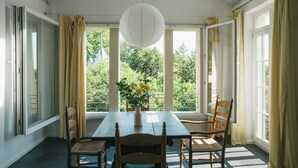 A room with a wooden table and chairs, a vase with flowers, and large windows with curtains. - Historic carriage house overlooking Havel (Werder (Havel))