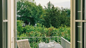A wooden deck with two chairs and a table, overlooking a garden with trees and bushes. - Historic carriage house overlooking Havel (Werder (Havel))