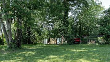 Une cour verdoyante avec des arbres, un abri de jardin et une petite construction.