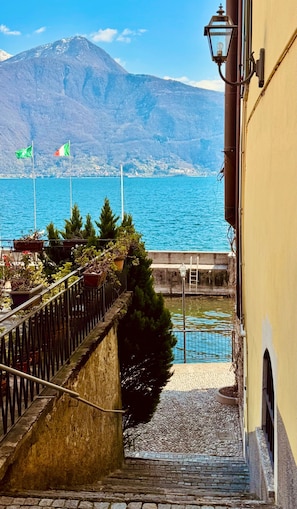 A staircase leading to a waterfront with a mountain in the background, a flag, and a lamp post. - Mansarda Spadone Attic (Musso)