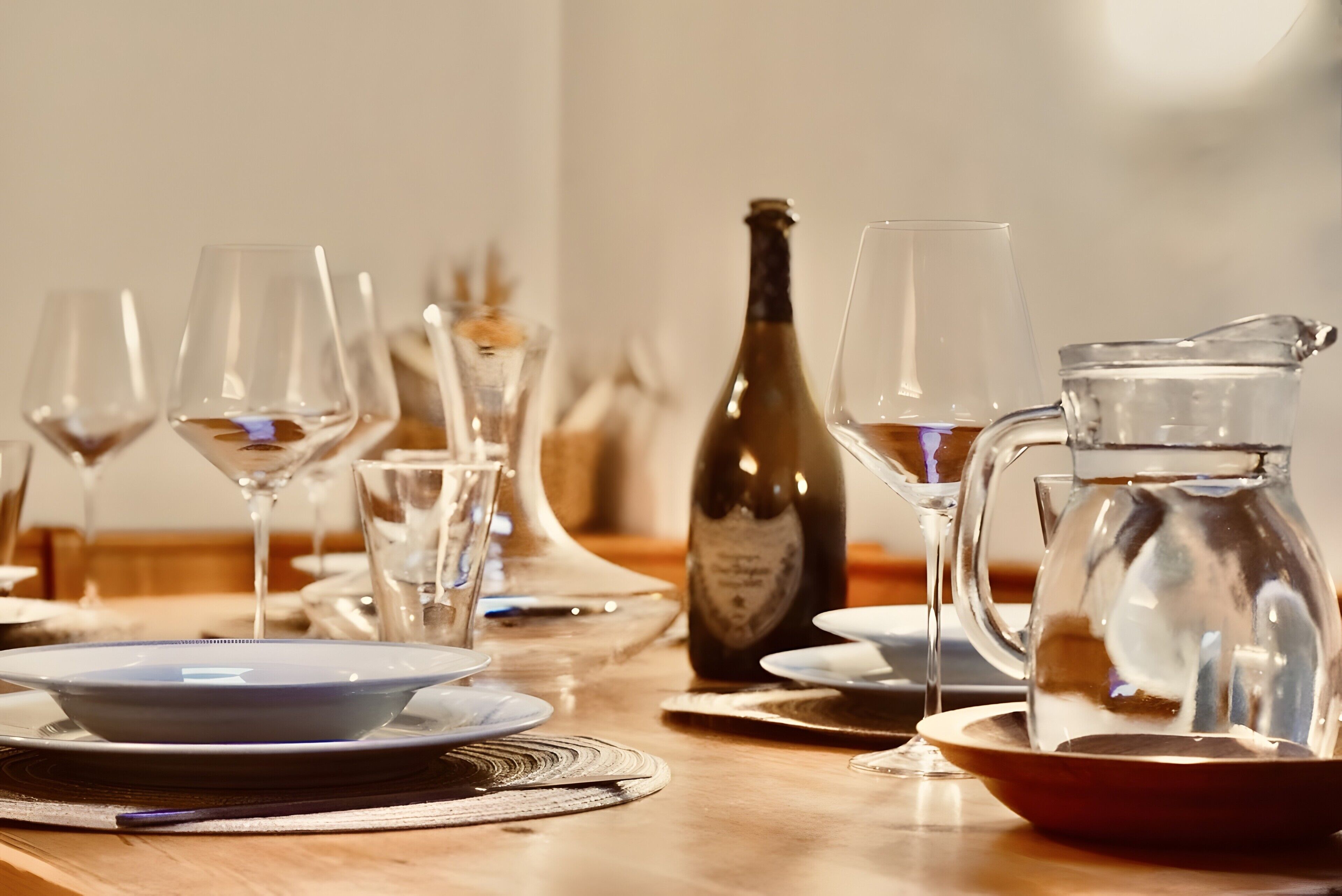 Una mesa de comedor lista con copas de vino, una botella y una jarrón.