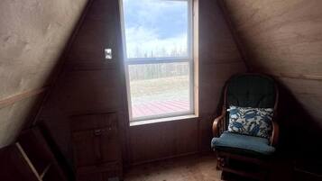 A small attic room with a window, a chair, and wooden walls.