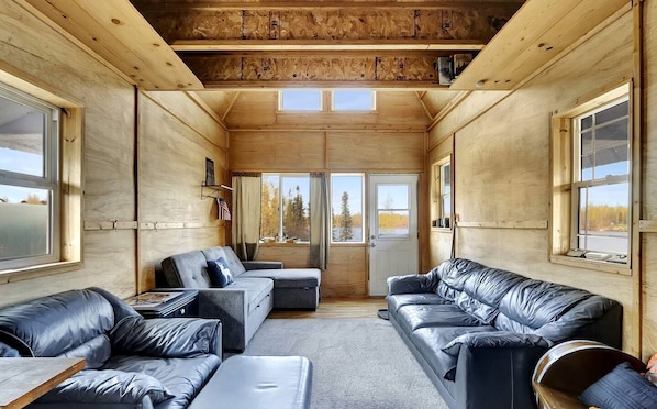 Un interior de cabaña con techo de madera, ventanas amplias y sofás de cuero.