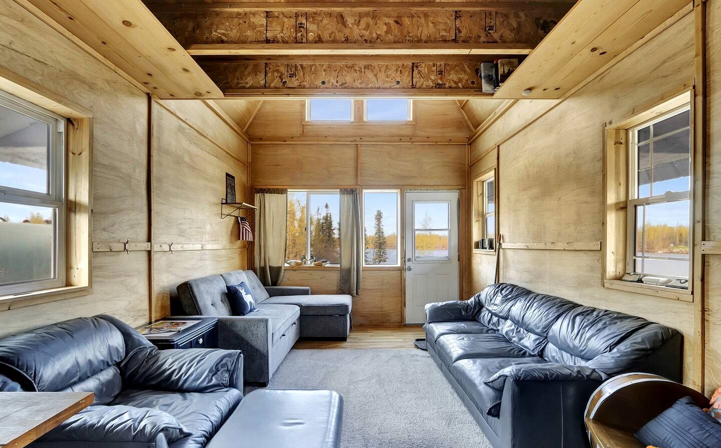 A cabin interior with a wooden ceiling, large windows, and leather sofas.