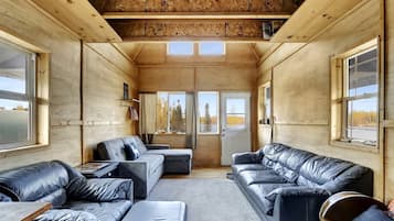 A cabin interior with a wooden ceiling, large windows, and leather sofas.