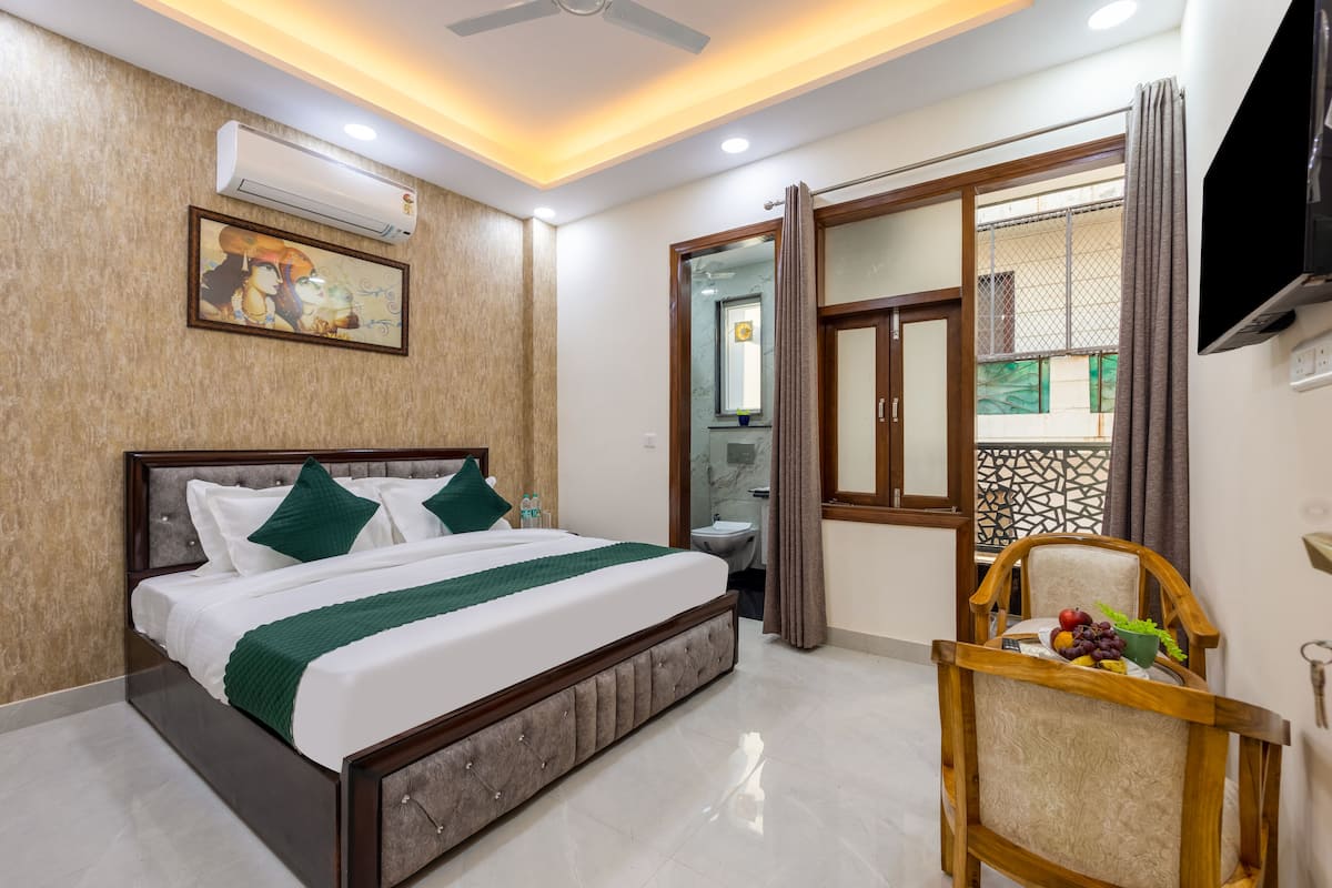 A hotel room with a bed, a chair with fruit, a TV, and an air conditioning unit.