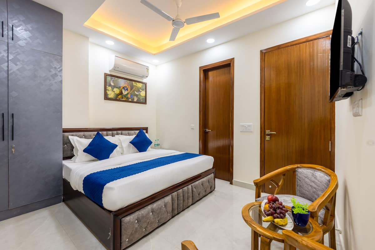 A bedroom with a bed, a ceiling fan, a TV, a wooden door, and a small table with fruits.