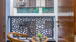 Un balcón con una silla y mesa de madera, una barandilla metálica decorativa y vistas a un edificio con varios balcones.
