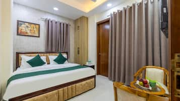 A hotel room with a bed, a nightstand, a chair with a tray table, curtains, a ceiling fan, and a wall-mounted TV.