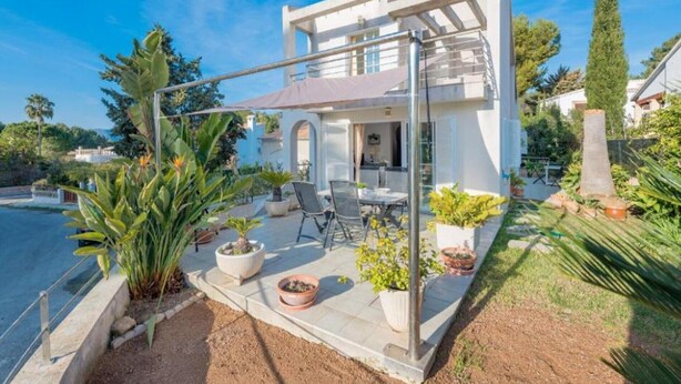 Een modern huis met een terras, buitenmeubels en plantenpotten.
