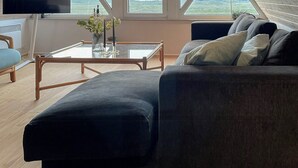 Ein modernes Schlafzimmer im Loft-Stil mit schrägem Dach, großen Fenstern, einem Flachbildfernseher, einer Couch und einem Couchtisch.