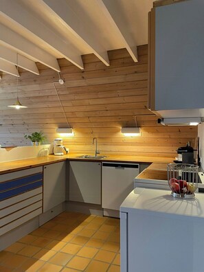 Eine moderne Küche mit Holzbalken, Pendelleuchten, einem Geschirrspüler und einer Obstschale.